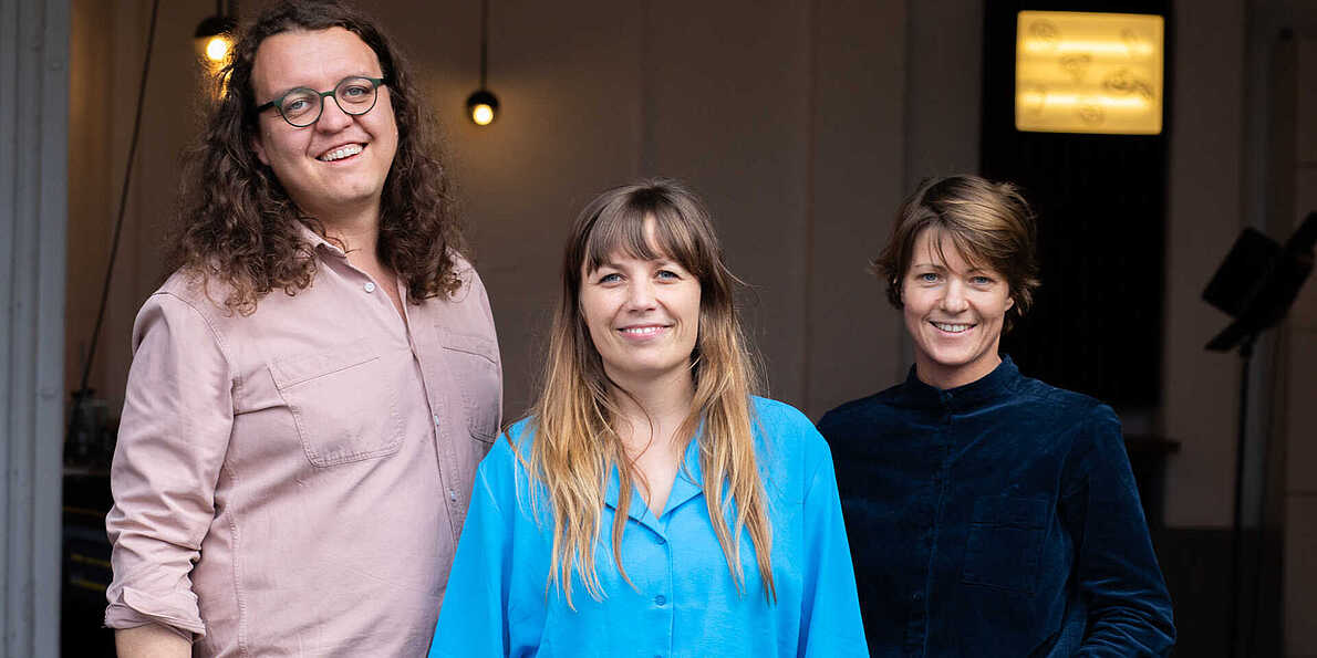 Das Bild zeigt die drei Gründer*innen. Links steht Anselm Stählin, dann Tanja Engel und rechts von ihr Paula Süveges