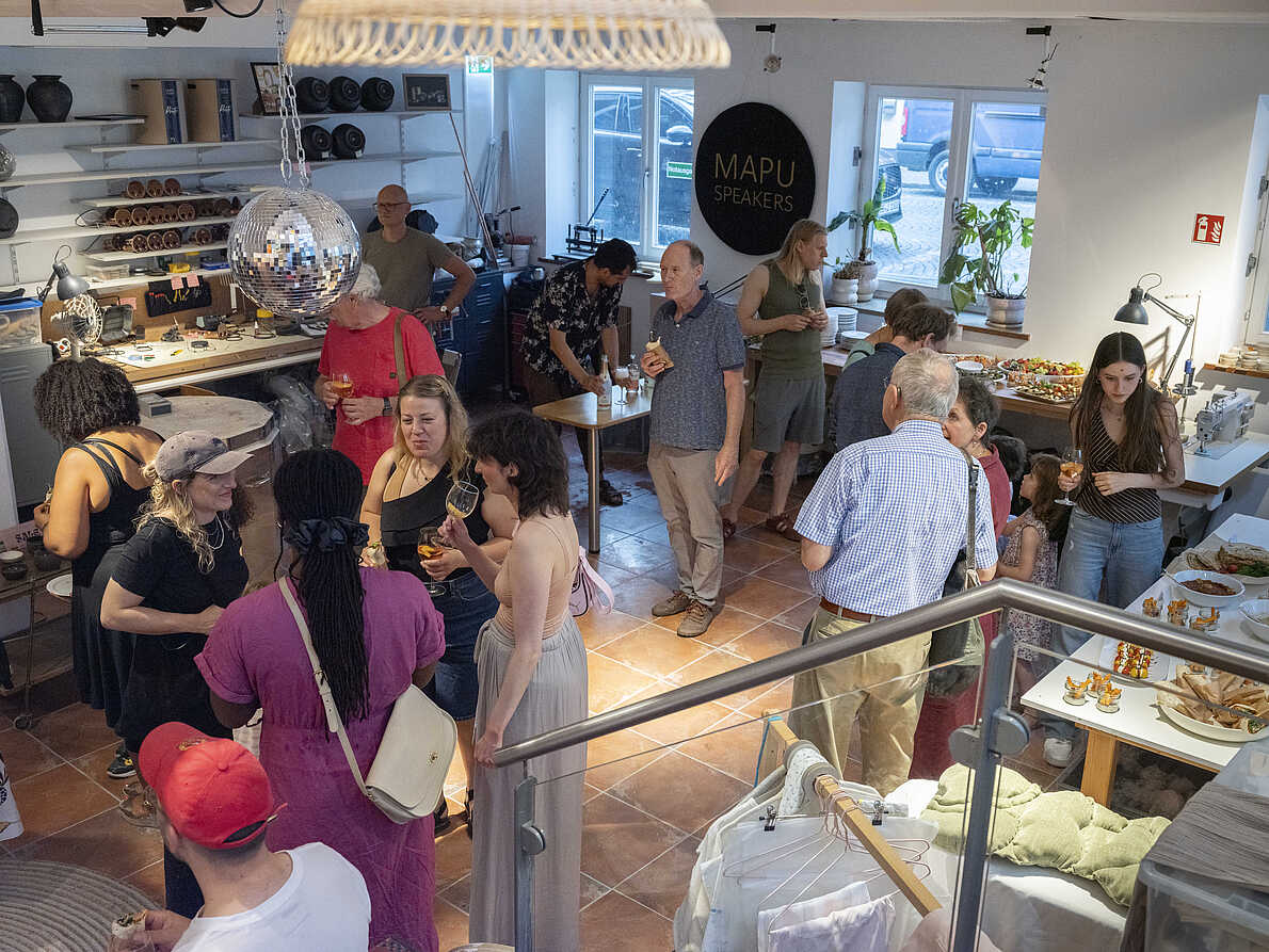 Impression der Eröffnung der Ausstellung "Different Futures Make A Dialogue". Viele Menschen in einem Raum, sie essen, trinken und unterhalten sich.