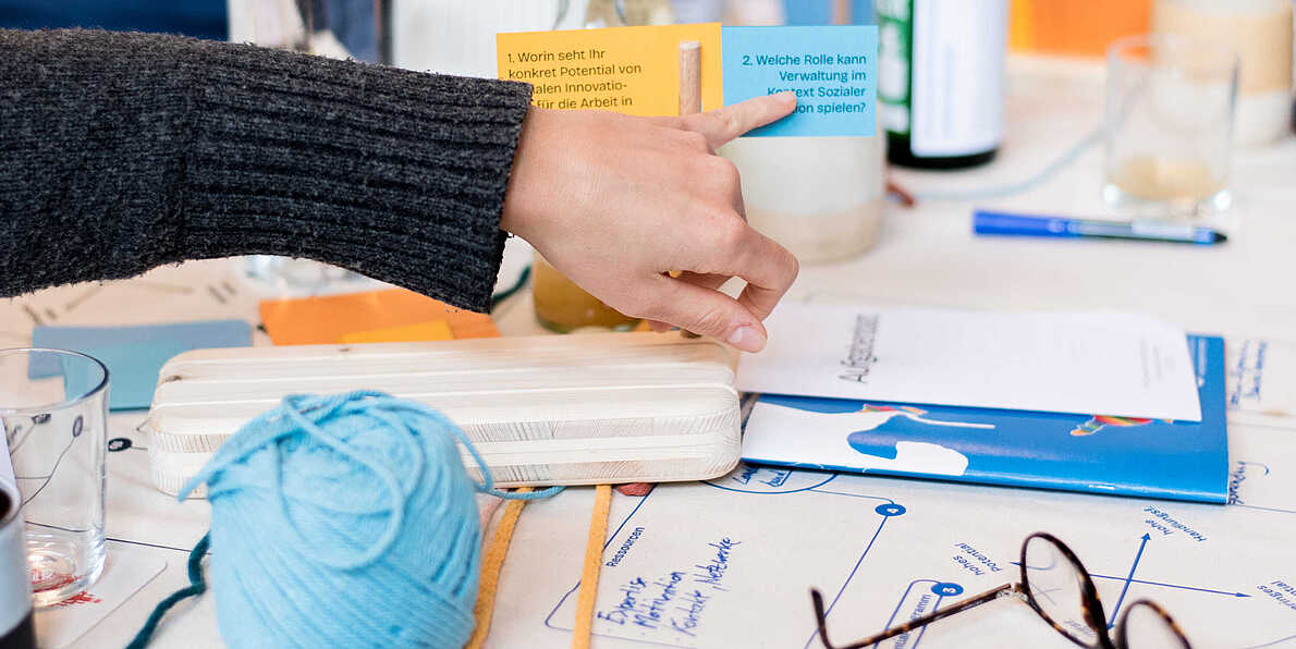 Eine Hand zeigt auf ein Fähnchen mit der Aufschrift "Welche Rolle kann Verwaltung im Kontext sozialer Innovation spielen?".