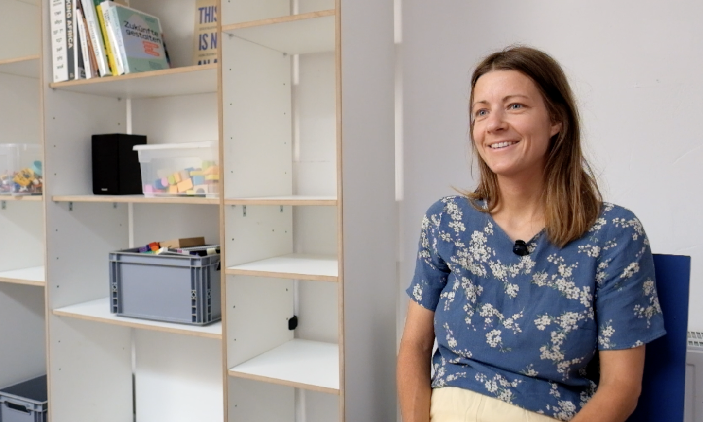 Paula sitzt auf einem Stuhl und schaut lächelnd nach vorn.